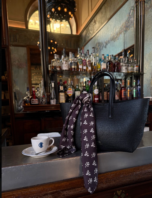 Black ALVEA leather tote with a patterned silk scarf tied to its handle at a café